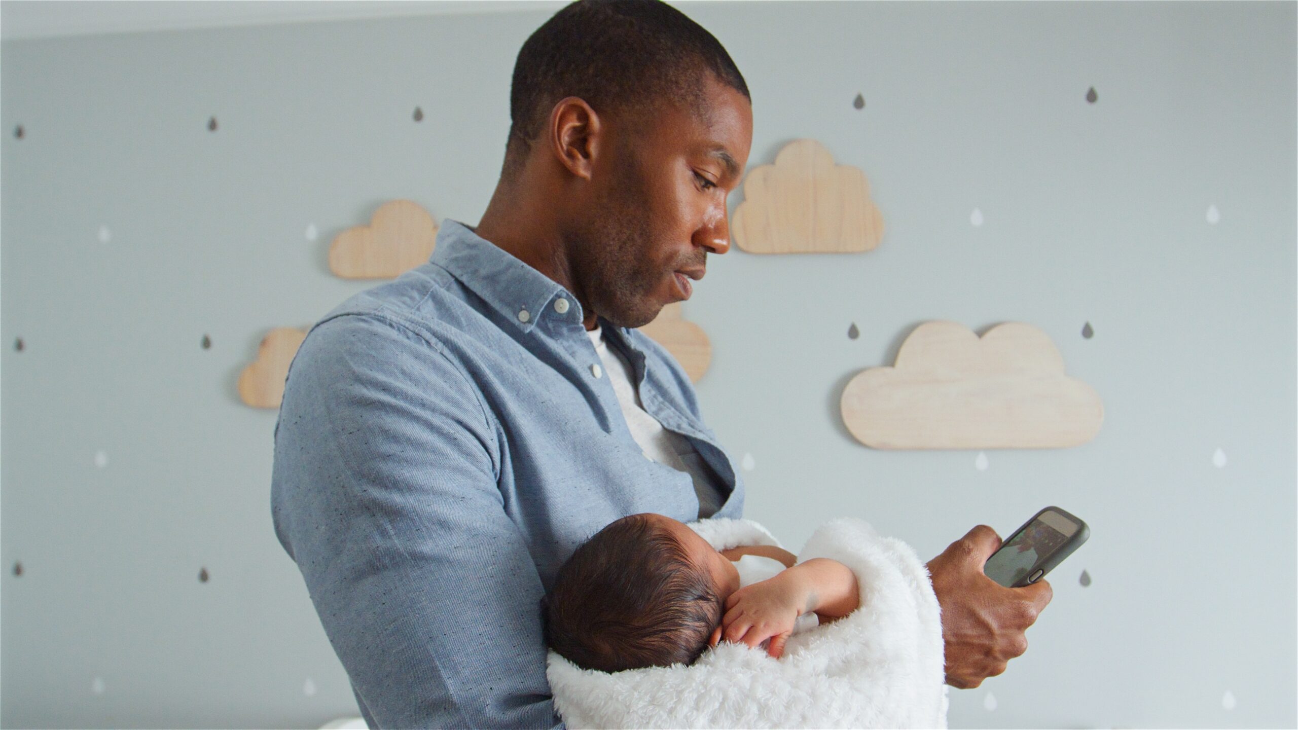 Father checking phone while holding newborn